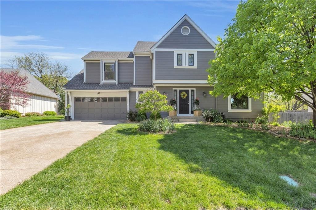 view of front of property with a front lawn, driveway, a shingled roof, an attached garage, and fence