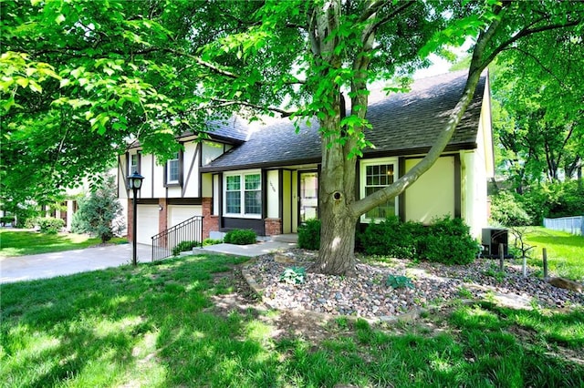 split level home featuring an attached garage, roof with shingles, asphalt driveway, a front lawn, and brick siding