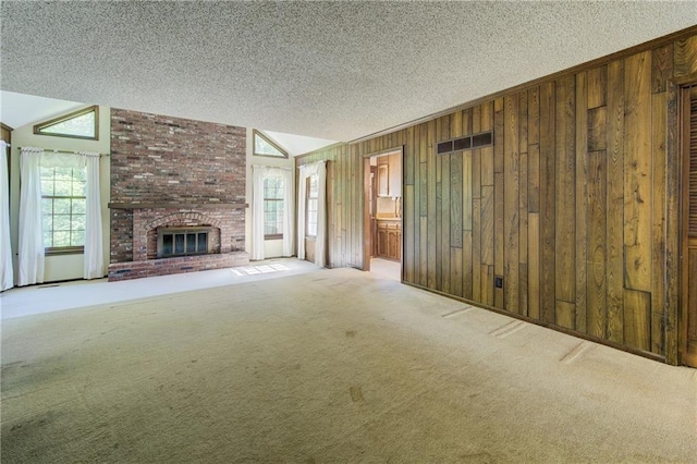 unfurnished living room featuring a textured ceiling, wood walls, carpet, lofted ceiling, and a fireplace