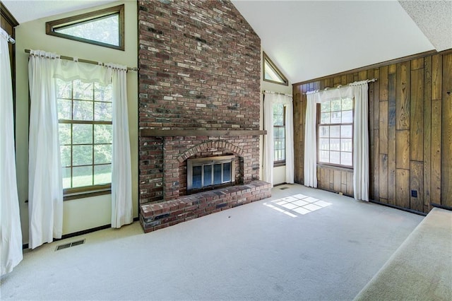 unfurnished living room featuring carpet, healthy amount of natural light, wooden walls, high vaulted ceiling, and a brick fireplace