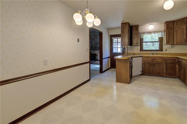 kitchen with white dishwasher, a sink, a textured ceiling, light countertops, and a chandelier