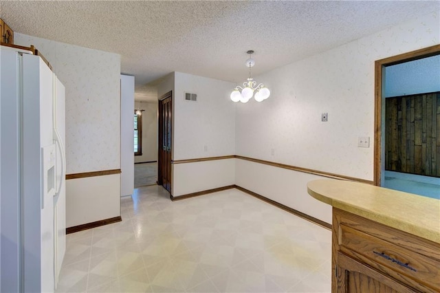 unfurnished dining area featuring light flooring, a textured ceiling, a chandelier, baseboards, and wallpapered walls