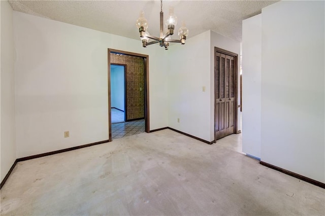 carpeted empty room featuring a chandelier, baseboards, and a textured ceiling