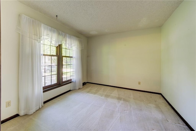 spare room with light carpet, a textured ceiling, and baseboards