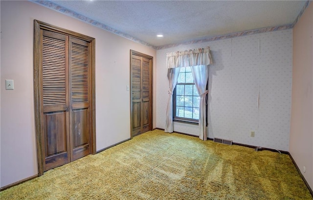 unfurnished bedroom featuring multiple closets, light carpet, a textured ceiling, and recessed lighting