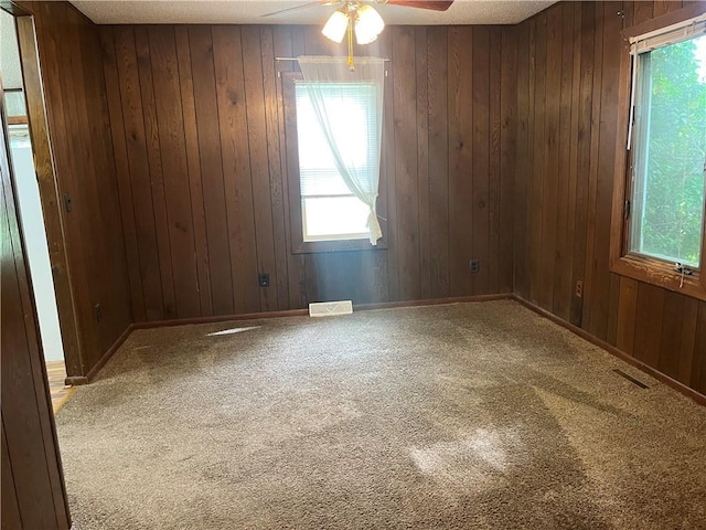empty room featuring a ceiling fan, carpet, and wooden walls