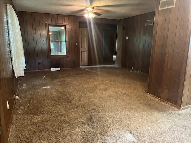 carpeted spare room featuring visible vents, wood walls, and ceiling fan