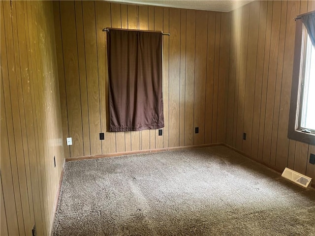empty room with visible vents, wood walls, and carpet floors