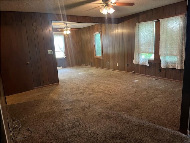carpeted empty room featuring a ceiling fan, a textured ceiling, and wooden walls