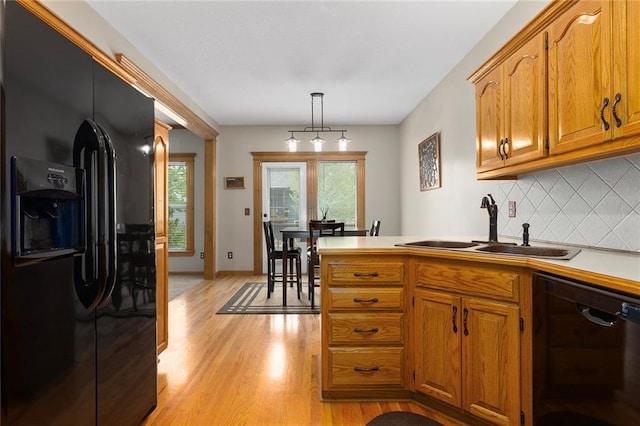kitchen with brown cabinetry, tasteful backsplash, a sink, light wood finished floors, and black appliances
