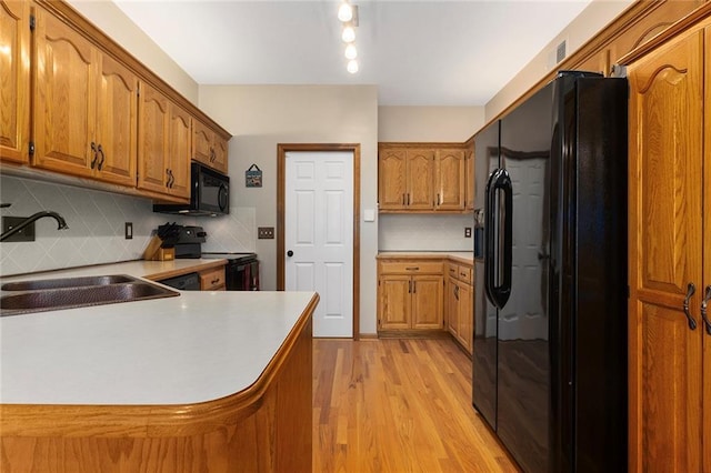 kitchen with light wood-style flooring, brown cabinetry, a sink, and black appliances