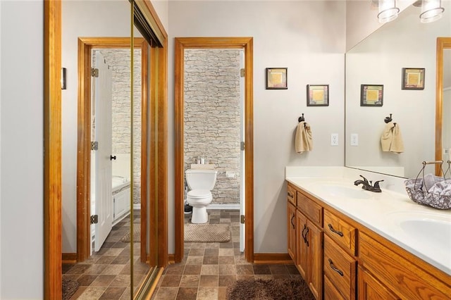full bath with a sink, toilet, double vanity, baseboards, and stone finish flooring