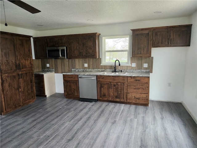 kitchen with light wood finished floors, a textured ceiling, appliances with stainless steel finishes, and a sink