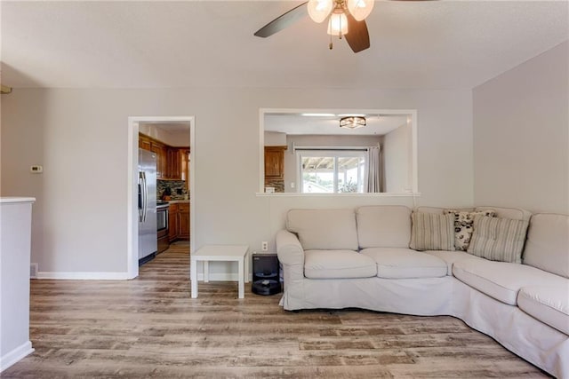 living room with light wood-type flooring, a ceiling fan, and baseboards