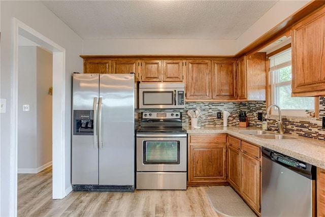 kitchen featuring appliances with stainless steel finishes, a sink, light wood-type flooring, light countertops, and brown cabinetry