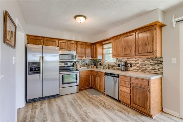 kitchen featuring stainless steel appliances, a sink, light wood-type flooring, light countertops, and a textured ceiling