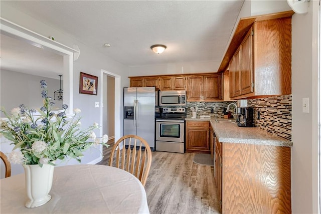 kitchen featuring appliances with stainless steel finishes, brown cabinetry, light countertops, light wood finished floors, and backsplash