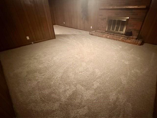 4926 Mockingbird Ln, Saint Joseph, MO 64506 - unfurnished living room featuring carpet flooring, a brick fireplace, and wood walls