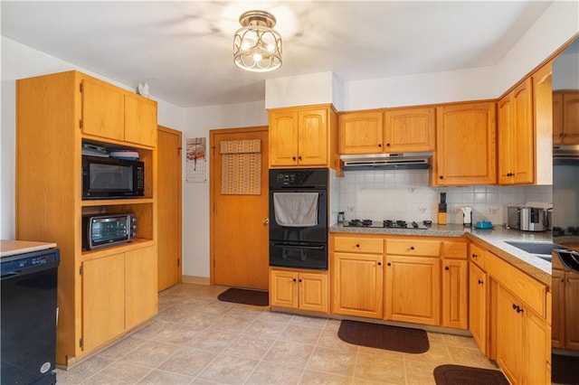 kitchen with light countertops, black appliances, decorative backsplash, under cabinet range hood, and a warming drawer