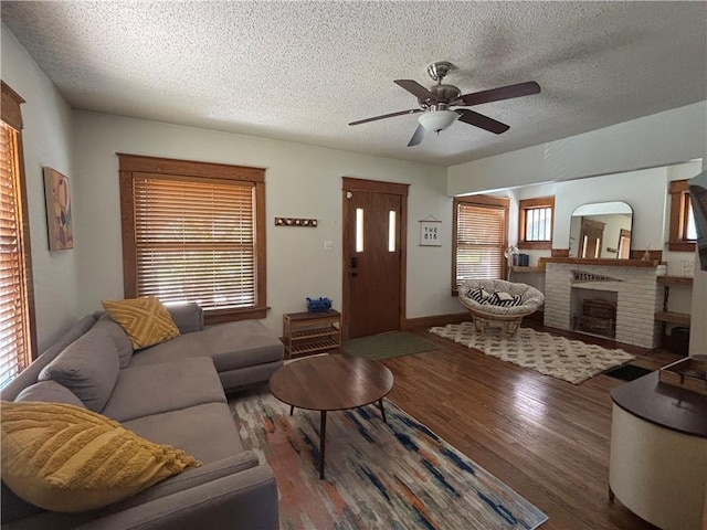 4019 Holly St, Kansas City, MO 64111 - living room featuring wood finished floors, a textured ceiling, ceiling fan, and a brick fireplace