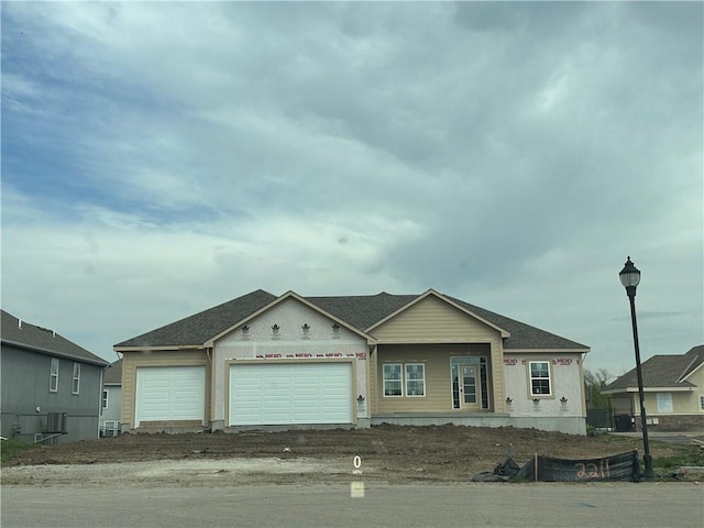 unfinished property with an attached garage, roof with shingles, and central AC unit
