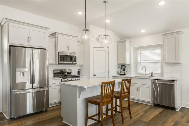 kitchen featuring dark wood-style flooring, appliances with stainless steel finishes, tasteful backsplash, a center island, and a sink