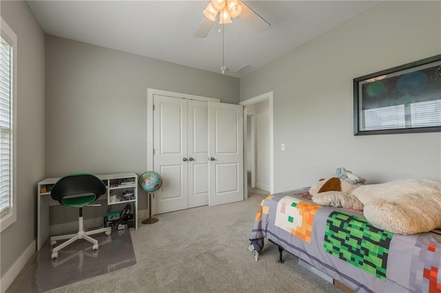 carpeted bedroom featuring a ceiling fan, baseboards, multiple windows, and a closet