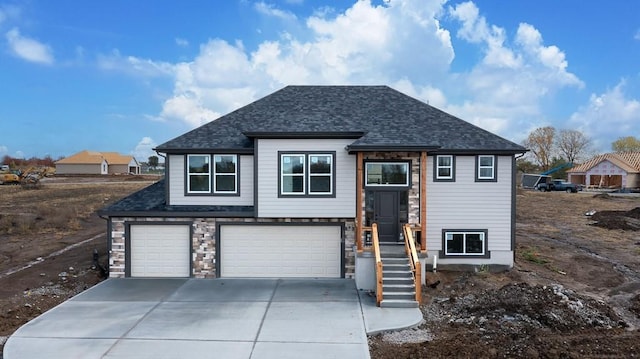 bi-level home featuring concrete driveway, stone siding, a shingled roof, and a garage
