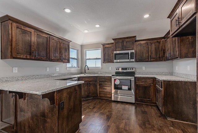 kitchen with dark wood finished floors, stainless steel appliances, dark brown cabinets, a sink, and a peninsula