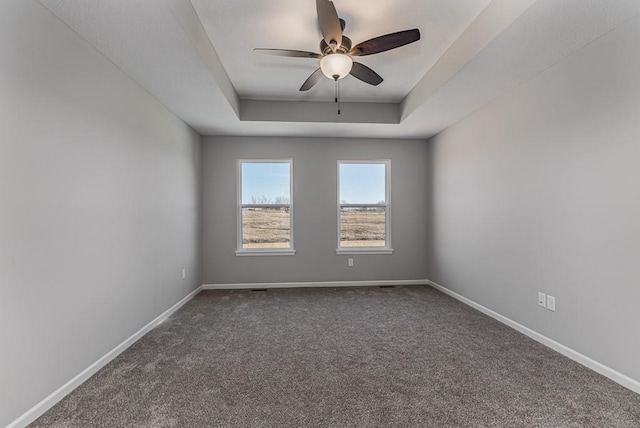 spare room featuring a raised ceiling, baseboards, dark carpet, and ceiling fan