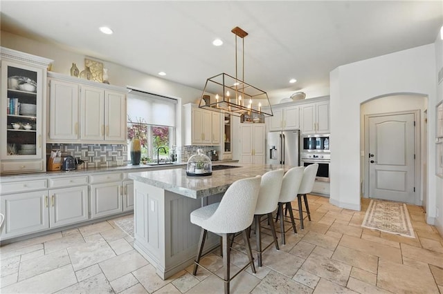 kitchen with decorative backsplash, a breakfast bar area, a kitchen island, glass insert cabinets, and stainless steel appliances