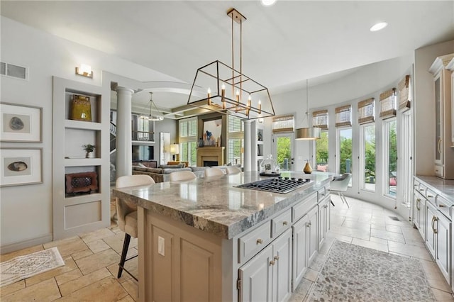 kitchen featuring visible vents, a fireplace, stainless steel gas cooktop, light stone counters, and stone tile floors