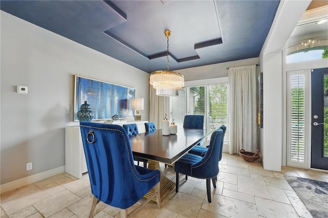 dining space with an inviting chandelier, a raised ceiling, baseboards, and stone tile flooring