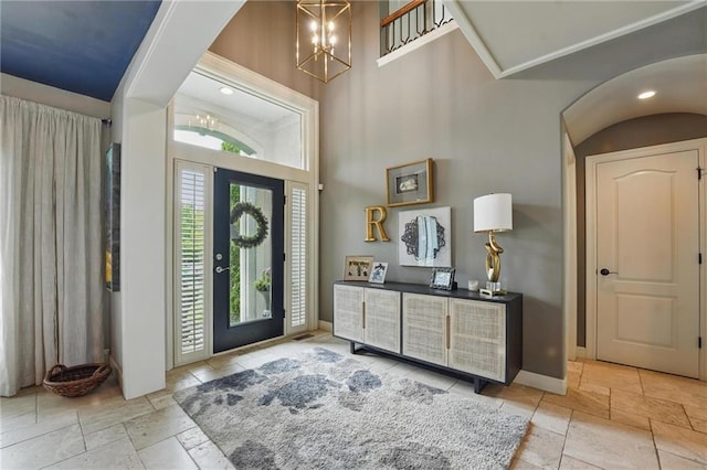 foyer featuring stone tile flooring, baseboards, a high ceiling, and a notable chandelier