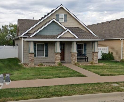 craftsman inspired home featuring a porch, roof with shingles, fence, and a front yard