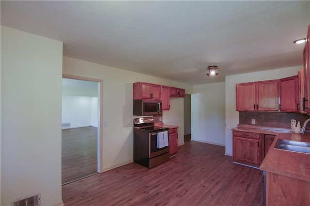 502 W Broadway St, Higginsville, MO 64037 - kitchen featuring appliances with stainless steel finishes, a sink, dark wood-style flooring, backsplash, and baseboards