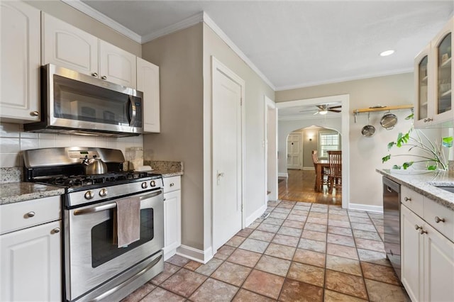 7227 Jefferson St, Kansas City, MO 64114 - kitchen featuring appliances with stainless steel finishes, baseboards, arched walkways, stone tile flooring, and crown molding
