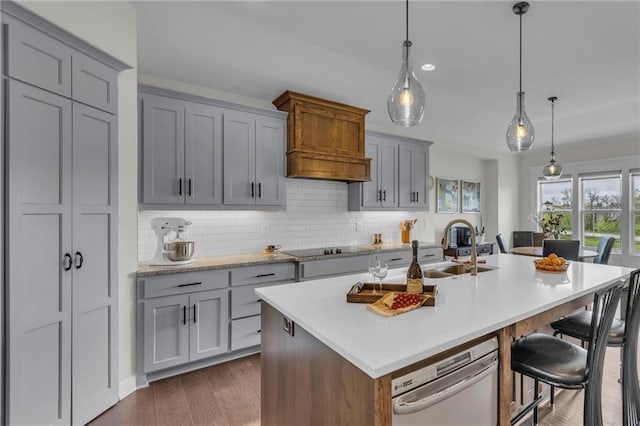 kitchen featuring a sink, light countertops, decorative backsplash, gray cabinetry, and a center island with sink