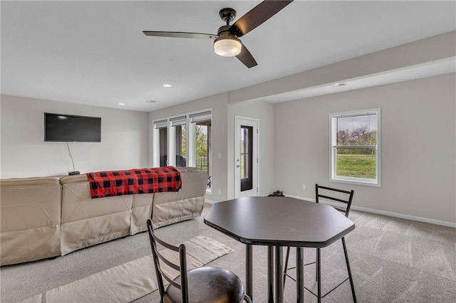 living room featuring baseboards, ceiling fan, light colored carpet, and a wealth of natural light