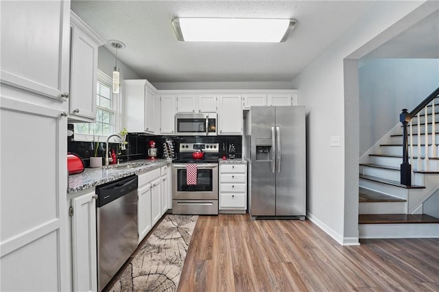 kitchen featuring appliances with stainless steel finishes, a sink, white cabinetry, light wood-style floors, and backsplash
