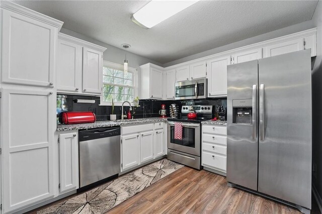 kitchen featuring stainless steel appliances, a sink, white cabinets, tasteful backsplash, and a textured ceiling