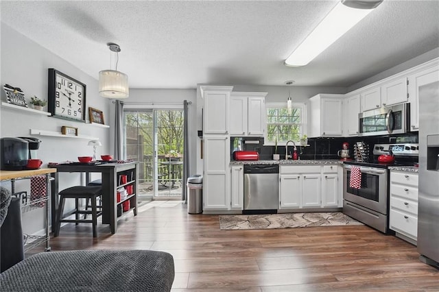 kitchen featuring stainless steel appliances, a sink, white cabinets, backsplash, and hanging light fixtures
