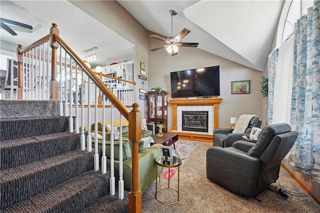 living room featuring a tiled fireplace, vaulted ceiling, a ceiling fan, and stairs