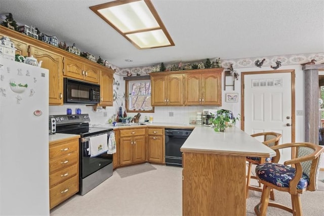 kitchen with a peninsula, light countertops, a breakfast bar area, and black appliances