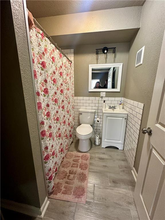 118-148 N Lawn Ave, Kansas City, MO 64123 - full bath featuring a textured wall, visible vents, toilet, wood finished floors, and tile walls