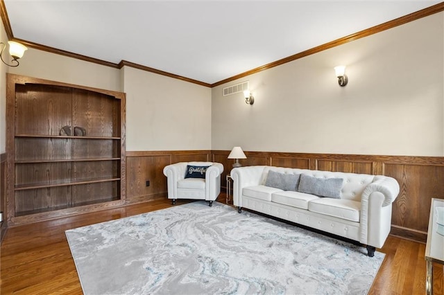 living room featuring visible vents, wainscoting, crown molding, and wood finished floors