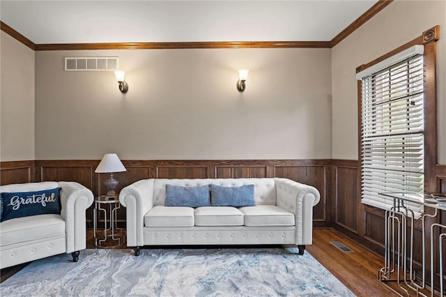 living area featuring visible vents, ornamental molding, wood finished floors, and a wainscoted wall