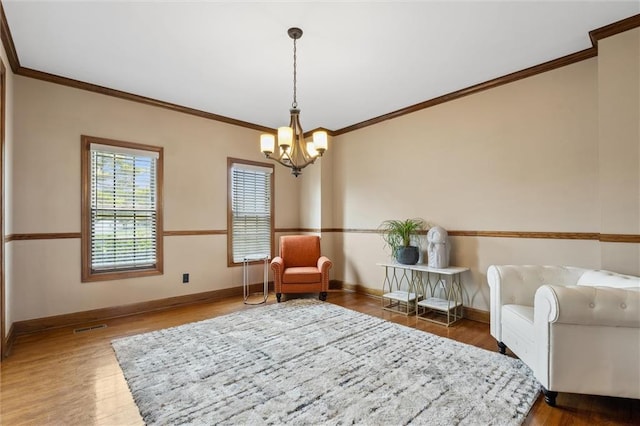 living area with baseboards, ornamental molding, wood finished floors, and a notable chandelier
