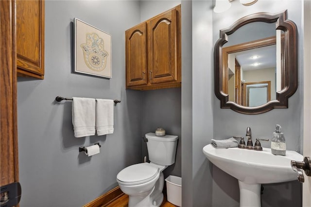 half bath with a sink, baseboards, toilet, and wood finished floors