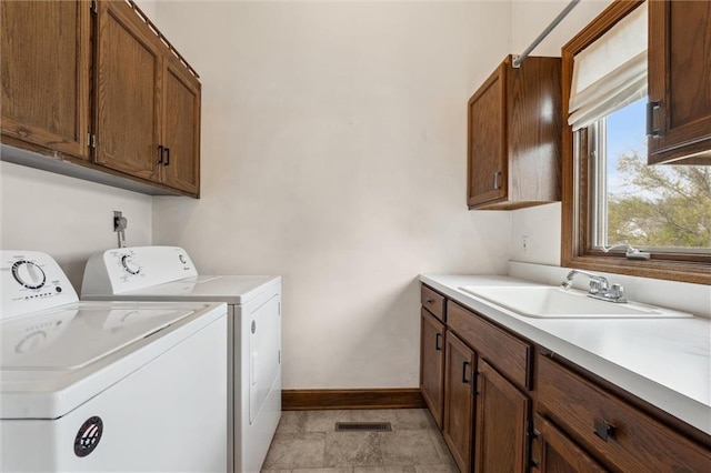 clothes washing area with visible vents, baseboards, washing machine and clothes dryer, a sink, and cabinet space